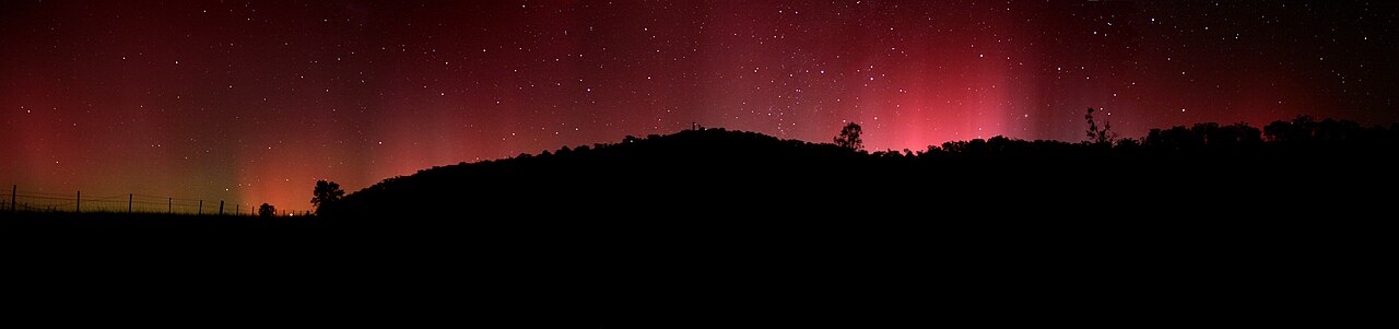 Red aurora australis over a hillside